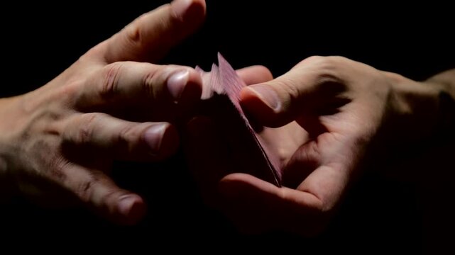 A deck of playing cards in the hands of a man on a black background.
The dealer shuffles the cards before the game.
Casino game and dealing cards.