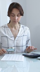 Accountant carefully examines financial documents, enlarges details with a magnifying glass,...