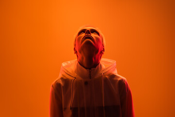 A person wearing a white hooded jacket is illuminated dramatically by vibrant orange and red lighting, resulting in a striking and impactful portrait showcasing creative lighting techniques and