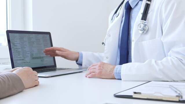 Doctor reviewing digital test results with patient, discussing health findings on laptop screen during clinical consultation. Medicine and health care concept.