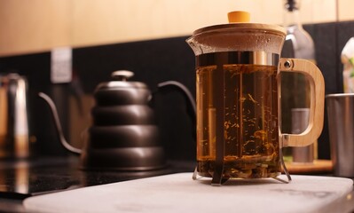 A French press filled with brewing herbal tea sits on a kitchen counter. The glass and wood design...