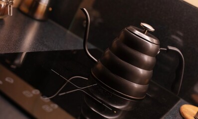 A matte black gooseneck kettle with a thermometer sits on a glossy black stovetop in a modern...