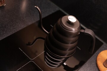 A matte black gooseneck kettle with a built-in thermometer is placed on a sleek black stovetop. Its...