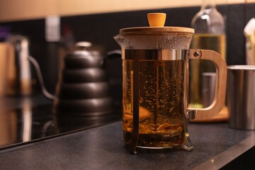 A French press filled with hot herbal tea sits on a kitchen counter. In the background, a matte...