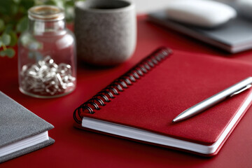 Red notebook, pen, and office supplies resting on desk