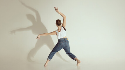 Inner voice. Young dancer captured from behind mid contemporary movement with dramatic shadow on...