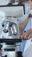 Female scientist wearing lab coat and protective glasses using a modern microscope in a laboratory...