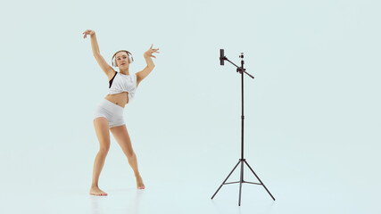 Learn through motion. Female dancer in white performing in front of phone on tripod with joyful...