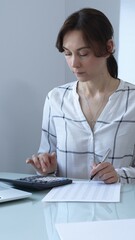 Female professional calculating finances, reviewing paperwork, tracking business expenses with...