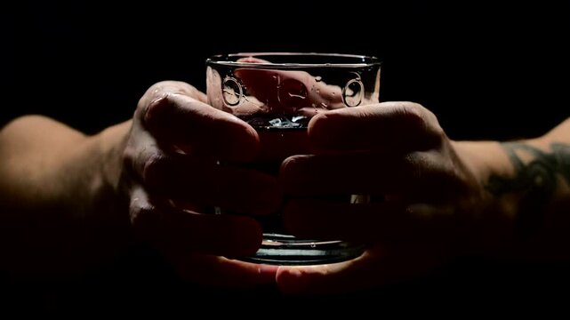 A sick man with tremors in his hands spills water from a tsakana on the floor and does not control his body due to severe tremors.
Parkinson's disease in an elderly man on a black background