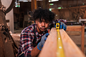 Skilled African American Construction Worker Measuring Timber Plank in Sawmill Using Tape, Focused...