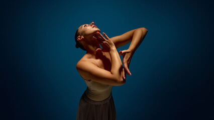 Strength and softness. Graceful woman performing close-up emotional hand gesture under spotlight on dark blue stage. Concept of expressive motion, stage choreography, vulnerability and dance theater. © Lustre Art Group 