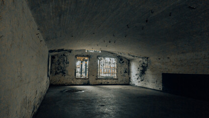 A dark, decaying prison cell with barred windows, stained walls, and ceiling hooks—evoking a...