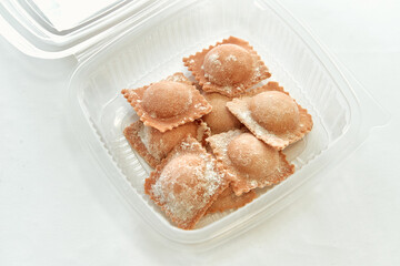 A Delicious Assortment of Fresh Pasta Ravioli Presented in a Clear Container, Showcasing the Appetizing Appeal of This Traditional Italian Dish