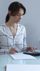 A professional woman calculates finances, checks documents, and accurately and carefully tracks...