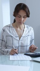 A professional woman calculates finances, checks documents, and accurately and carefully tracks...