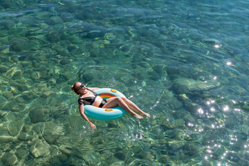 Woman relaxing on inflatable float in clear turquoise water, enjoying summer sunshine, surrounded...