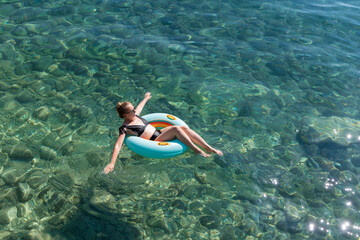Woman relaxing on a floating ring in clear turquoise water, enjoying a sunny day at the beach,...