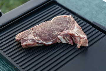 Freshly seasoned ribeye steak resting on a grill plate, ready for cooking, showcasing summer...