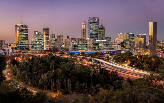 Fototapeta View of city lights dance across the skyline, reflecting in the modern architecture above lush greenery and winding roads, Perth, Western Australia, Australia.