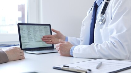 Doctor reviewing digital test results with patient, discussing health findings on laptop screen during clinical consultation. Medicine and health care concept.