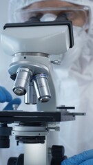 Close up of medical virologist in a hazmat suit, mask, and gloves, diligently working at a microscope in a laboratory researching viruses. Medicine and science concept