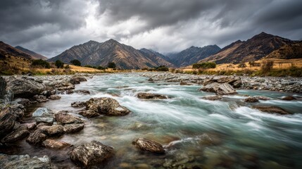A dramatic landscape featuring a flowing river, rocky terrain, and rugged mountains under a moody sky