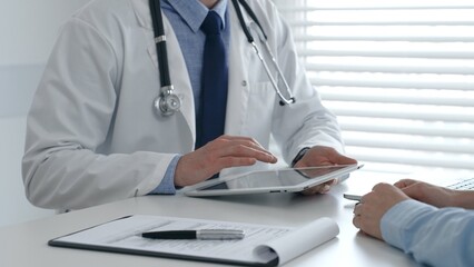Male doctor sharing information with patient on a digital tablet during consultation, enhancing...