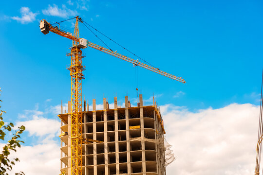 A building under construction with a tower crane rises against the blue sky. The building's frame is ready, workers continue construction.