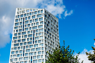 Obraz premium A modern building with white facades and balconies, surrounded by greenery, against the backdrop of a clear blue sky. The architecture emphasizes the style and comfort of the residential complex.