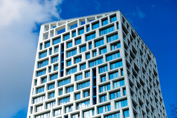 Fototapeta premium Modern building with geometric facade, snow-white walls, many windows, clear blue sky, stylish and harmonious view.