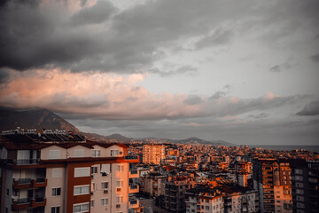 Alanya City skyline at sunset with clouds and mountains in the background overlooking urban...