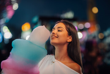 Happy young woman eating cotton candy at night in amusement park
