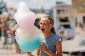 Excited girl holding large multicolored cotton candy at amusement park