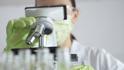 Close up of scientific precision involving green gloved hands adjusting microscope lens, blurred...