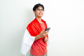 Happy Indonesian man holding national flag and using smartphone with a smile, celebrating...