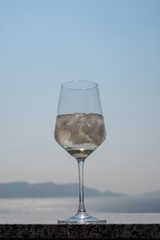 A wine glass with ice cubes stands on a balcony railing with a blue sky