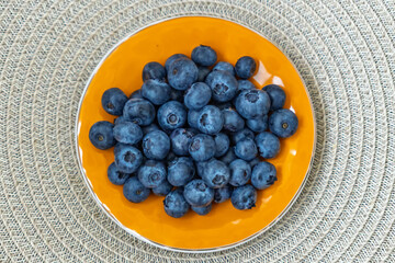 Heap of ripe juicy blueberries in a bowl on a round placemat. Concept of natural desserts, and diet food. Healthy raw food ingredient for a smoothie or snack, viewed from above