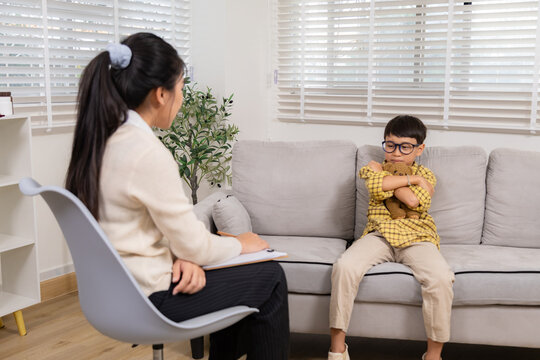 Therapy, child, counseling, psychologist, emotion shown through body language as young boy tightly hugs teddy bear while avoiding eye contact, expressing anxiety during mental health session, autistic