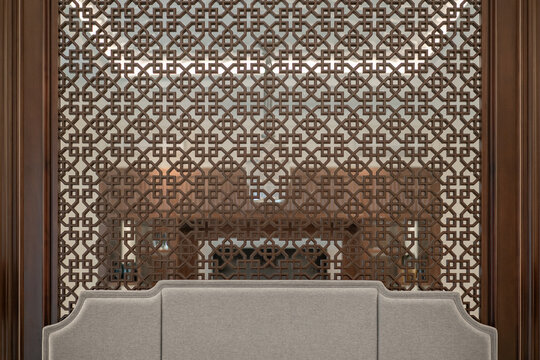 An intricate dark brown wooden lattice screen serves as a stunning headboard for a grey fabric bed. Symmetrical, classic, and luxurious bedroom design.