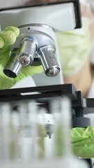 Close up of green gloved hands of a scientist adjusting a microscope in a laboratory, emphasizing...