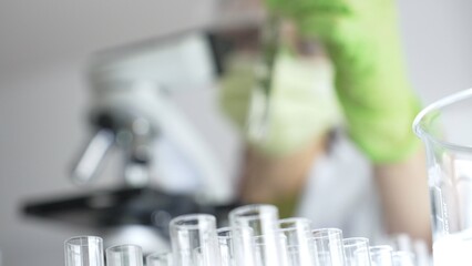 Close up of test tubes with a scientist analyzing plant samples in test tubes with a microscope in...