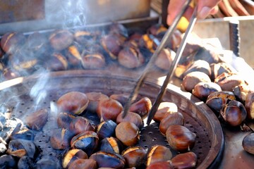 Chestnuts, a traditional Turkish street food. A close-up of a hand holding a chestnut with tongs. Smoke rises as the chestnuts roast over a charcoal fire. Winter.
