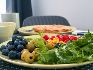 A colorful assortment of olives, corn, blueberries, fresh green leaves, and cherry tomatoes creates...