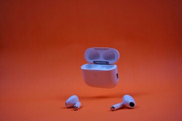 Modern Wireless Earbuds and Charging Case on Bright Orange Background