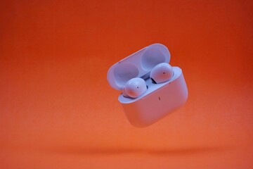 Modern Wireless Earbuds and Charging Case on Bright Orange Background