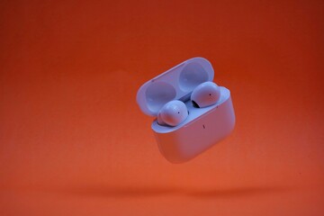 Modern Wireless Earbuds and Charging Case on Bright Orange Background