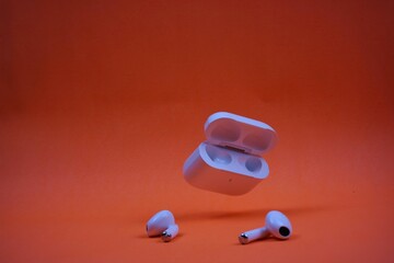 Modern Wireless Earbuds and Charging Case on Bright Orange Background