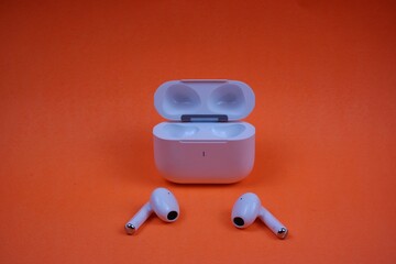 Modern Wireless Earbuds and Charging Case on Bright Orange Background