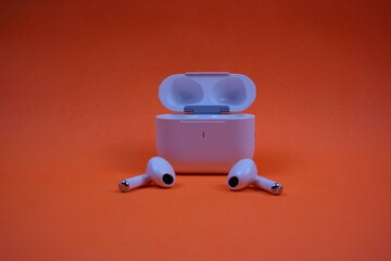 Modern Wireless Earbuds and Charging Case on Bright Orange Background